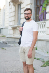 Handsome young man with beard wearing glasses, white t-shirt, beige shorts