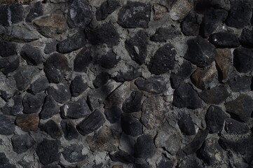 Photo of the texture. Black stone and concrete mortar. Illuminated by the direct rays of the sun.