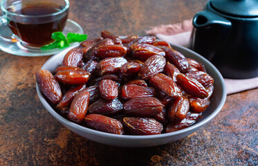 Sun-dried dates in a ceramic bowl and fruits scattered on a wooden table. Organic dried fruits.