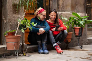 Fototapeta na wymiar Two female friends using a smart phone, sitting together in trendy city neighborhood