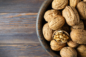 Walnuts in a plate on a brown wooden background. Nuts are a source of vegetable protein. Copy space. Flat top view.