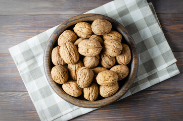 Walnuts in a plate on a brown wooden background. Nuts are a source of vegetable protein. Flat top view