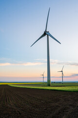 Wind turbines that produce sustainable green energy located on an agricultural field during a spring day at sunset. Vertical alignment. © Gabriel
