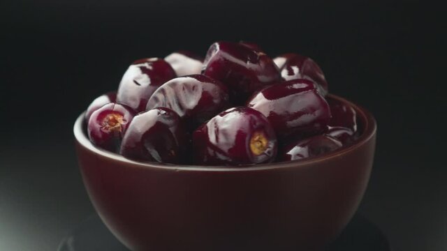 Juicy fruits of Mazafati dates in a wooden cup on a dark background rotate. Shooting from a tripod with studio lighting.