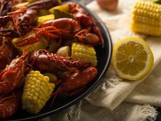 Fototapeta na wymiar On a white background, a black plate with boiled crayfish and corn. The lemon is bright yellow, cut in half. No people. Close-up. Detailed view.