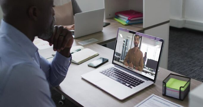 African american man having a video call with female colleague on laptop at office