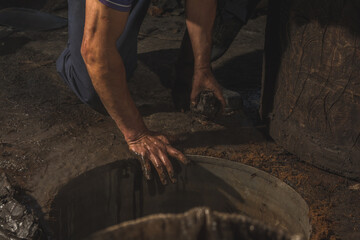 Mezcal master cooking the pineapple from the agave to extract the juice and convert it into mezcal, putting clay around the oven to seal it.
