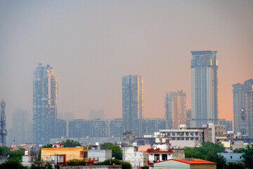 Naklejka premium Zoomed in shot showing glass skyscrapers multi story floor tall buildings on a rainy dawn lit from the side by orange sunshine showing the rapid growth of real estate property 