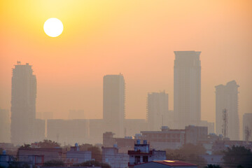sun rising over hazy foggy skyscrapers with multi floor tall buildings with smaller houses in the foreground in the city of bangalore hyderabad gurgaon and other indian cities