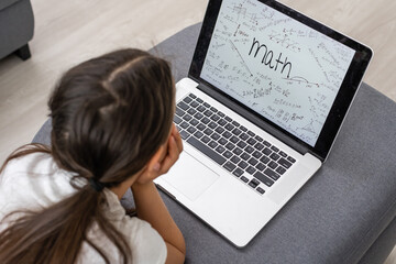 Bored little girl with laptop at home. Cute child doing homework on computer. Modern online education, communication and technology concept, copy space.