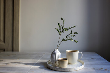two cups of coffee of different sizes for two on a tray on the table. Corrugated vase with dry...