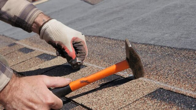 Laying of soft tiles. Bitumen roofing. Hammering nails with a hammer.
