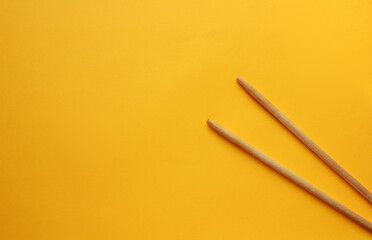 View from above on wooden chopsticks on a yellow background. Sticks are on the right side. Food appliances. Flat lay. Copy space