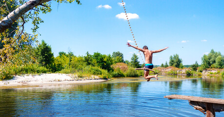 Young boy jumping into the river from wooden bridge. The teenager froze in the air above the water making a jump.