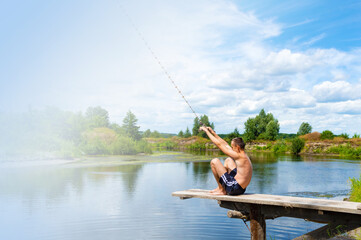 Fototapeta premium Boy teenager sits on a wooden bridge going to jump into the river from the swinging rope on sunny summer day. Copy space.