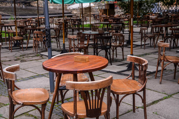 Fototapeta na wymiar Empty street cafe with small round tables and wooden chairs after rain at the cloudy day