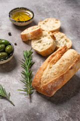 Italian fresh ciabatta bread with olive oil, olives and herb on rustic brown background. Top view, flat lay. Side view, selective focus.