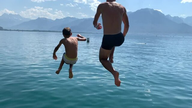 Father and son running at lake pier and jumping into water. people diving