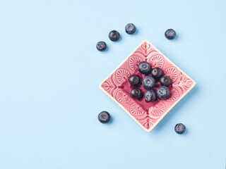Bowl of fresh blueberries and a strawberry on a blue and pink background