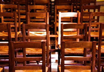 View on isolated old brown wood chairs with backrest in a row inside catholic empty church illuminated by natural sun light - Gassin, Cote d´Azur, France