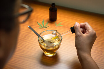 Woman pouring CBD oil in a natural infusion. Using CBD, natural remedy made with cannabis.