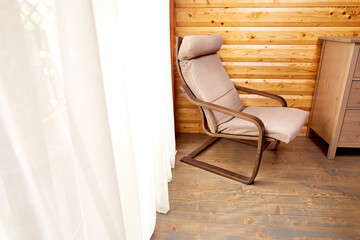 Fototapeta na wymiar interior of wooden house. Comfortable chair near window with elegant curtains in room