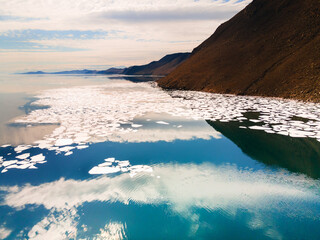 Melting ice floes on the shore of Baikal lake in spring. Aerial drone view. Mountains and sky are...