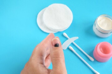 Injured finger on the hand with a hematoma under the nail on blue background with ointment and...