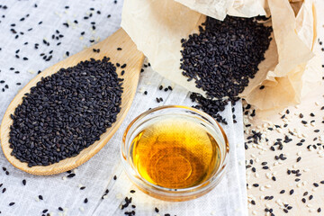 Black sesame seeds in a wooden spoon and oil on light background in the kitchen