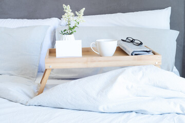 Breakfast in bed stationery mockup scene. Blank greeting card mockup, cup of coffee, newspaper and glasses on tray. White vase with small flowers. Valentine's day breakfast, lifestyle concept.