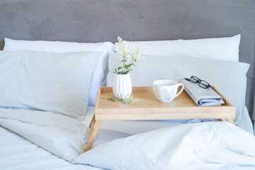 Fototapeta na wymiar Breakfast in bed stationery mockup scene. Cup of coffee, newspaper and glasses on tray. White vase with small flowers. Valentine's day breakfast, lifestyle concept.