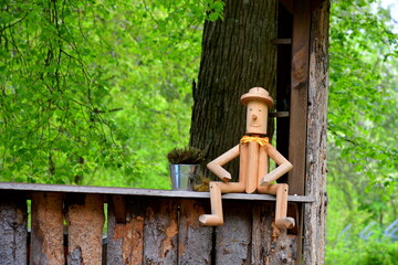 A close up on a small wooden figurine made out of small logs and branches sitting on a wooden fence next to a large tree seen in the middle of a dense forest or moor on a Polish countryside