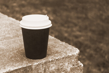 A cardboard cup of coffee sits on a stone curb. Take coffee outside.
