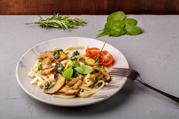 Udon with mushrooms and spinach in a plate on a concrete background next to a fork.