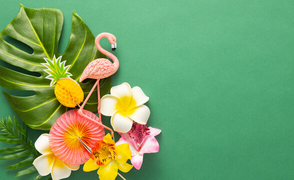 Exotic jungle summer frame. Summer beach party concept. Pink flamingo, tropical leaf monstera and orchid flowers on green background. Flat lay, copy space.