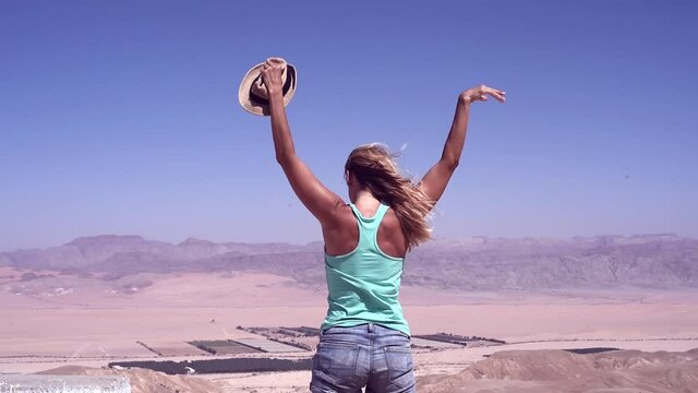 Young slim girl in hat stand back side in yellow mautain in endless expanse of desert. woman happy to feel freedom, careless, everything achievable look forward, sucksecfull. wind blowing hair.