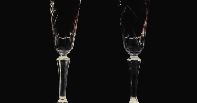 On a black background, on the table, there are two crystal glasses with red wine. The camera moves from bottom to top.