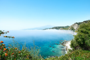 View of the gulf of Giardini Naxos coverd by fog with Mount Etna in background. Beauty in Sicily as a tourist attraction. Season on mediterranean sea. Ionian sea.