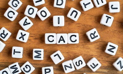 Small white and black bead cubes on wooden board, letters in middle spell CAC - Customer acquisition cost concept