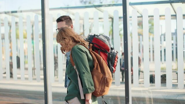 Handsome happy Caucasian young man tourist with backpack walking in town meeting his girlfriend with suitcase in positive mood, travelling together, travellers on vacation, travel concept