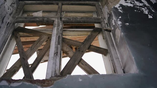 The window of an abandoned house is boarded up from the inside creating a barrier. The camera shoots close-up in motion from the inside