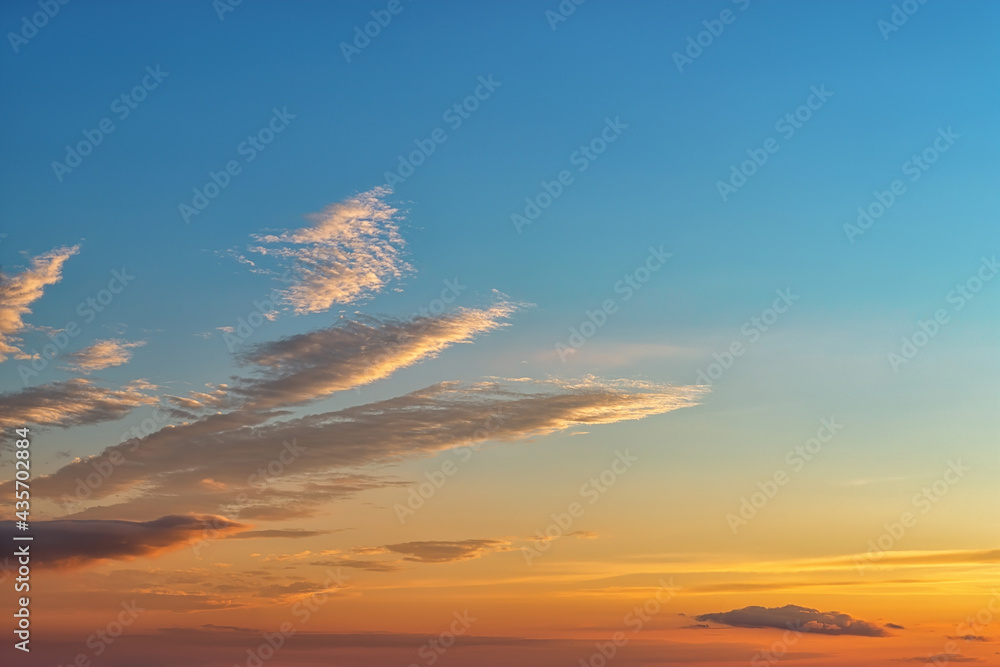 Wall mural calm golden blue sunset sky with few long clouds at left. the rays of the setting sun gilded the clo