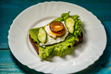 sandwich of bread, salad, cucumber, plum and scrambled eggs on a white plate