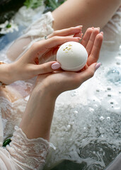 White bath bomb with jasmine in the hands of the girl in the bathroom