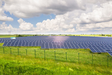 Aerial view of solar power plant on green field with protective wire fence around it. Electric...