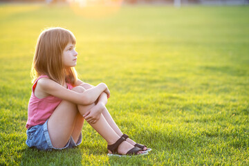Fototapeta premium Young happy child girl resting while sitting on green grass lawn on warm summer day.