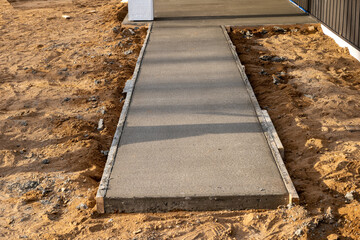 Recently poured concrete sidewalk and adjacent dirt, at construction site.