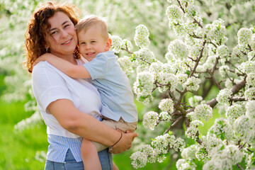 mother holds her young son in a flowering spring garden. parental love and care