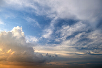 Dramatic sunset landscape with puffy clouds lit by orange setting sun and blue sky.