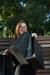 Girl with black shopping bags on bench in park. Vertical frame. Black Friday